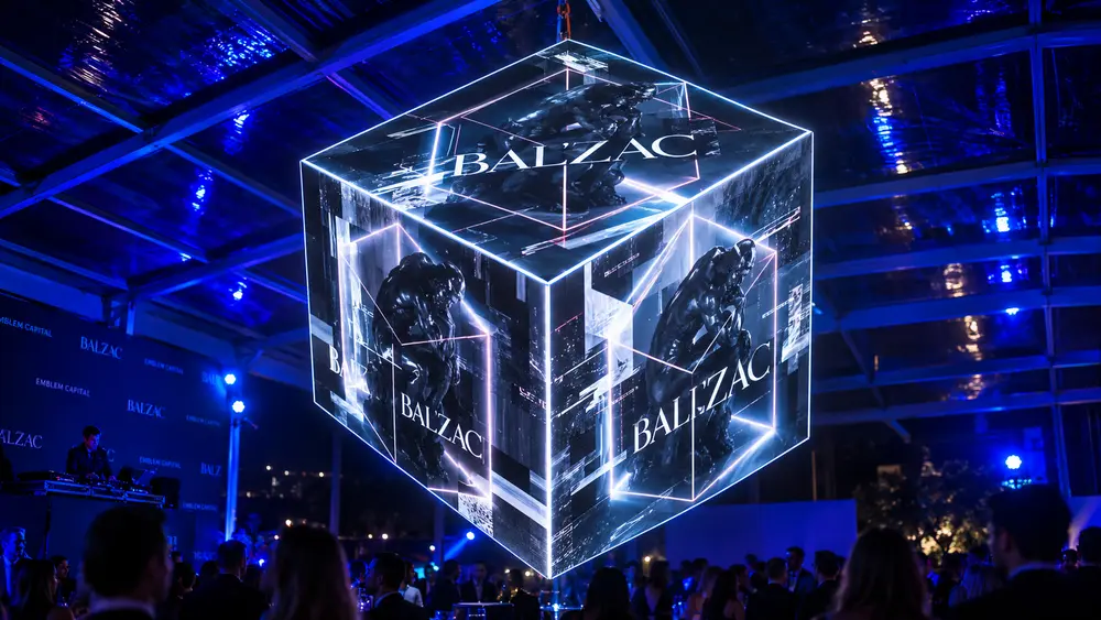 Cubo luminoso suspendido en un evento, con la escultura de Rodin y el logo Balzac proyectados en sus caras