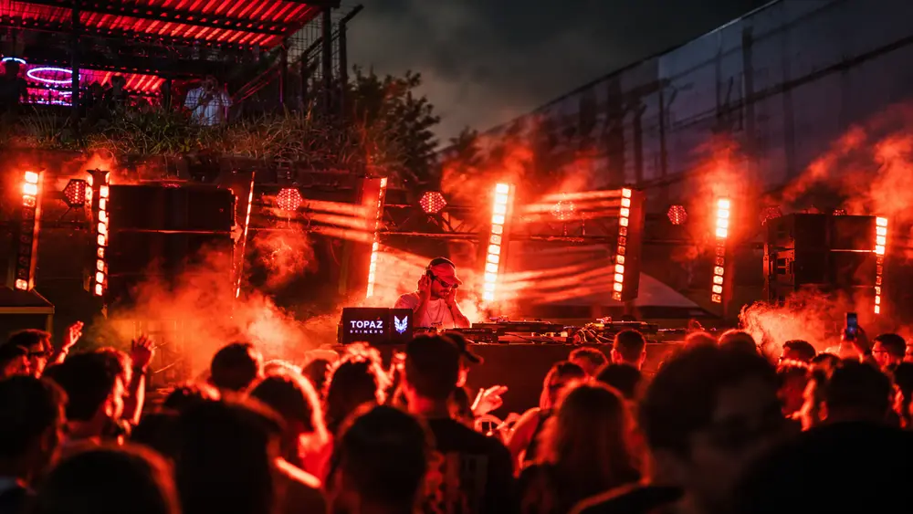 DJ en un escenario al aire libre con iluminación roja y público